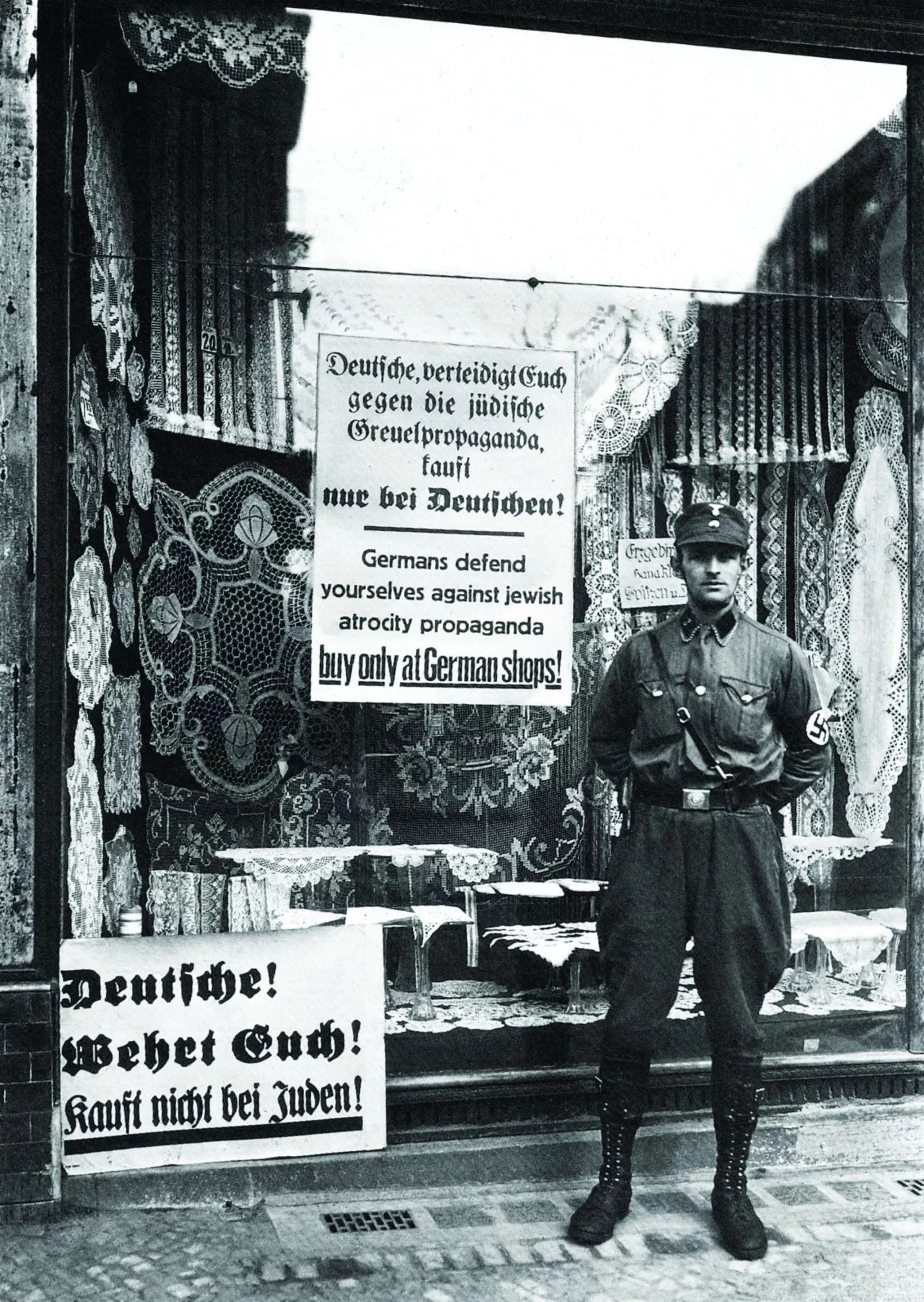 An SA brownshirt stands outside a Jewish-owned shop in Berlin during the boycott of April 1, 1933. Signs in the shop window warn Germans not to buy from Jews.