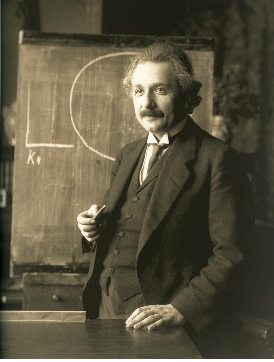 A 1921 photographic portrait of Albert Einstein standing beside a blackboard