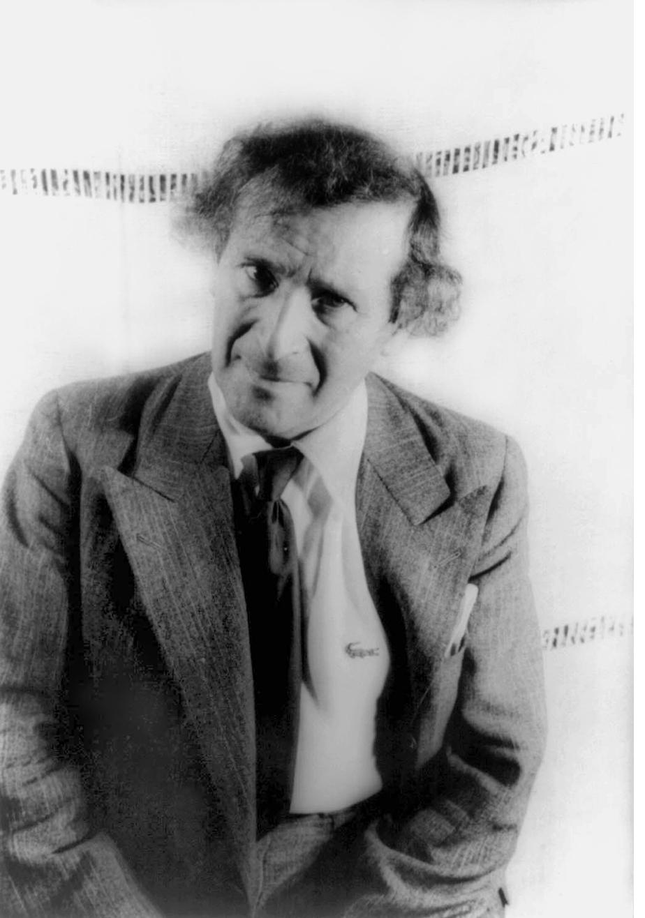 A 1941 portrait photograph of Marc Chagall standing in a tweed suit and tie, hands in his pockets, against a light backdrop
