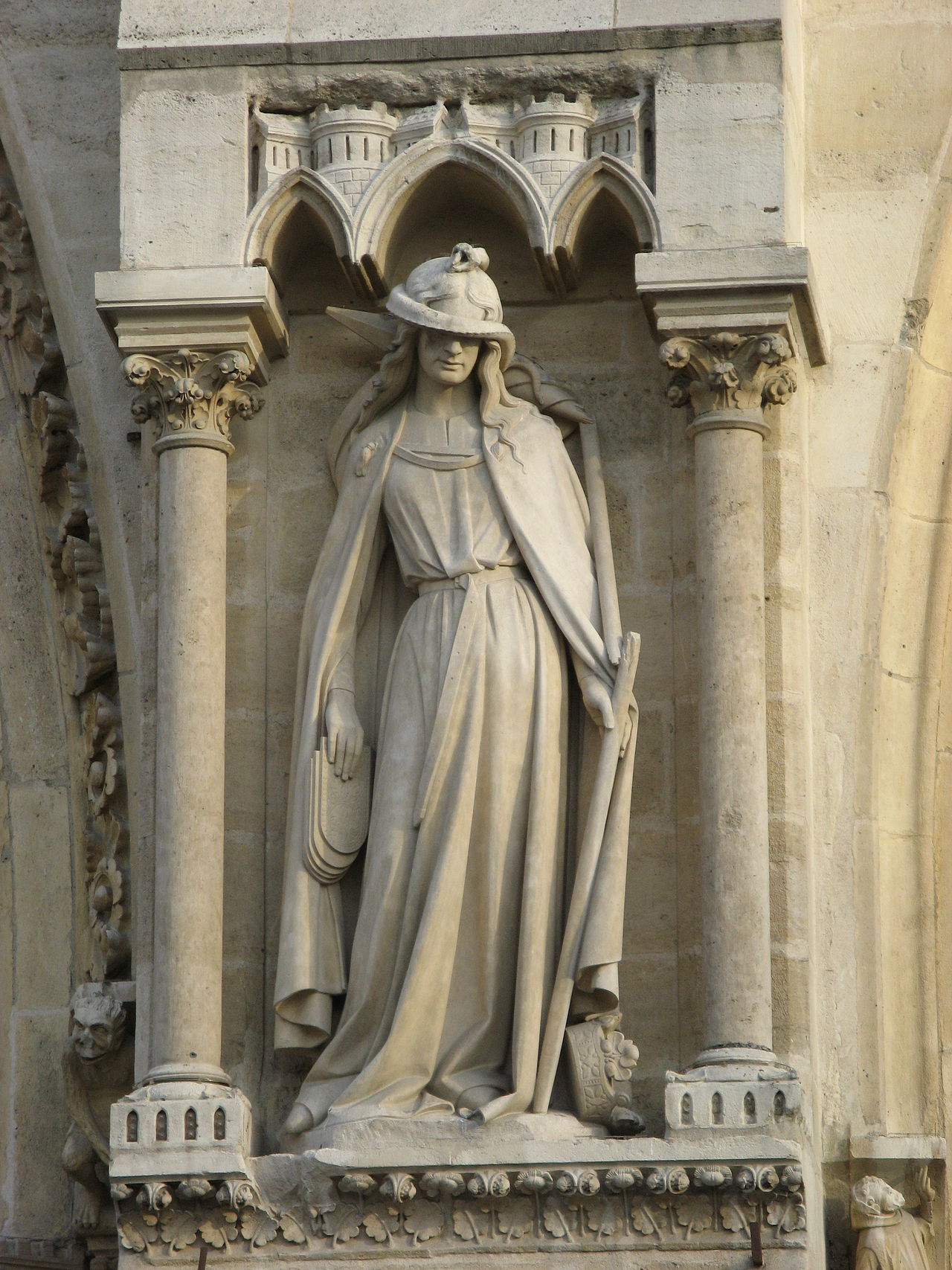 A stone statue of a woman, elegantly carved, standing with a serpent coiled across her eyes, holding a broken staff, with tablets slipping from her lowered hand.