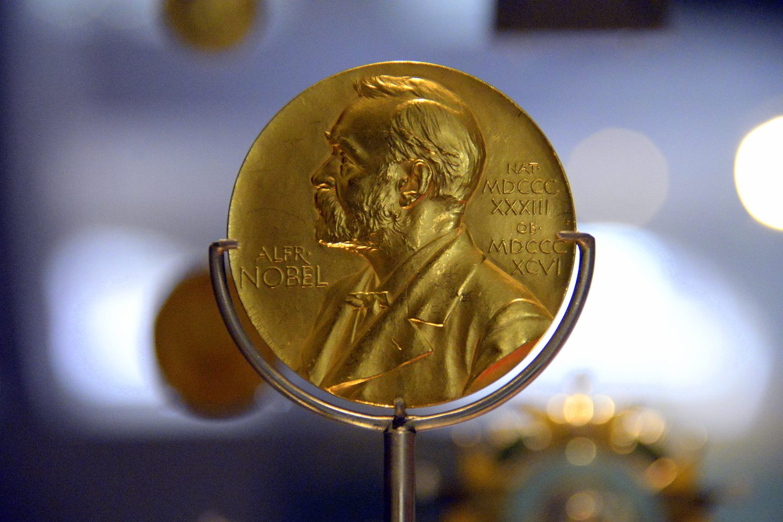 A gold Nobel Prize medal on a display stand: Alfred Nobel in profile, with his birth and death years inscribed in Roman numerals.