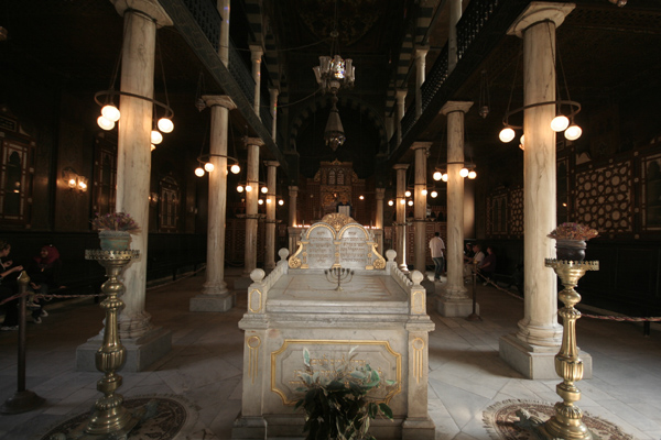 The marble interior of the Ben Ezra Synagogue in Cairo, with columns, hanging lamps, and a central raised bimah.