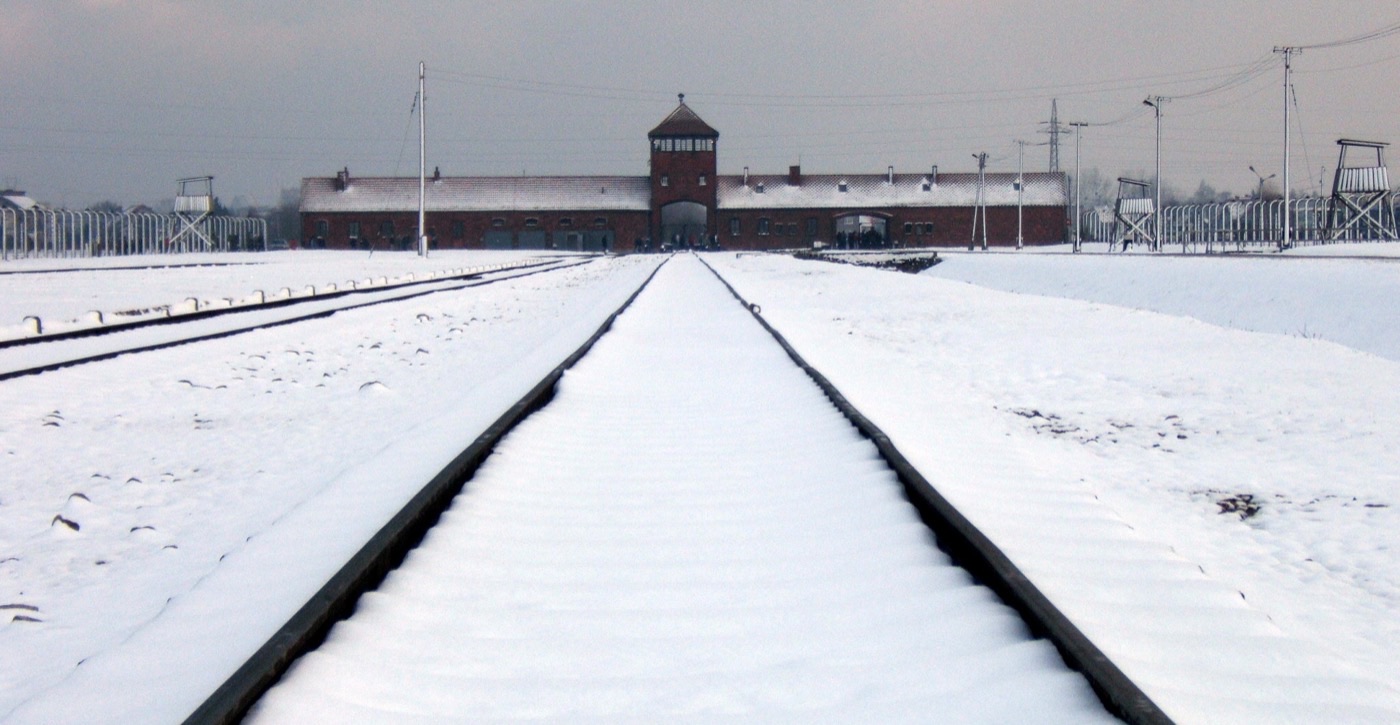 The main gate of Auschwitz II-Birkenau, a long brick guardhouse with the railway running through it into the camp.