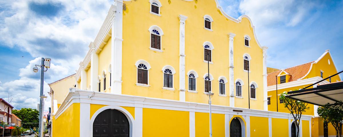 The bright yellow colonial facade of the Mikvé Israel-Emanuel synagogue in Willemstad, Curaçao, with white trim and a curved Dutch gable.