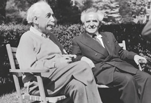 Two elderly men sitting in garden chairs outdoors: Albert Einstein in a light sweater on the left, and David Ben-Gurion, with his distinctive halo of white hair, on the right.