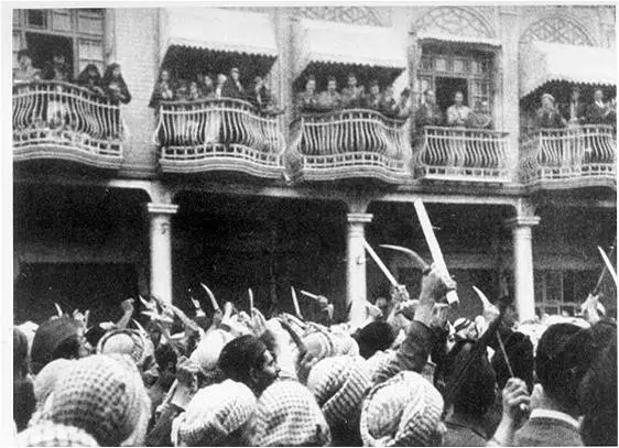 A crowd raising knives and daggers toward people standing on balconies above, during the 1941 Farhud pogrom in Baghdad.