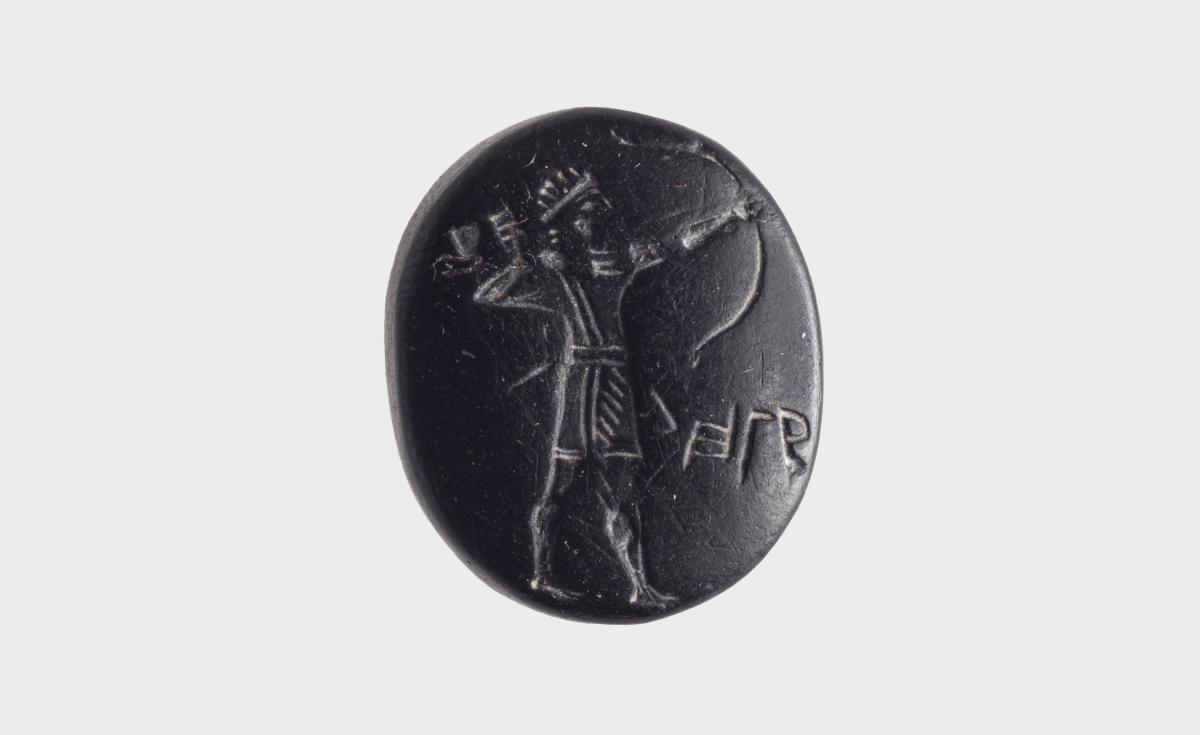 A small oval black stone seal engraved with a standing archer drawing a bow, with a short line of early Hebrew letters beside him.