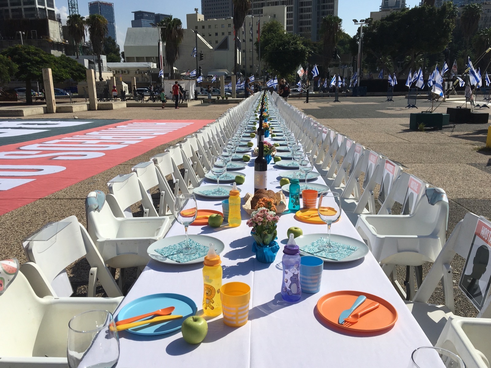 A long Shabbat dinner table set with empty chairs and place settings, one for each hostage, in the public square in Tel Aviv that became known as Hostages Square.