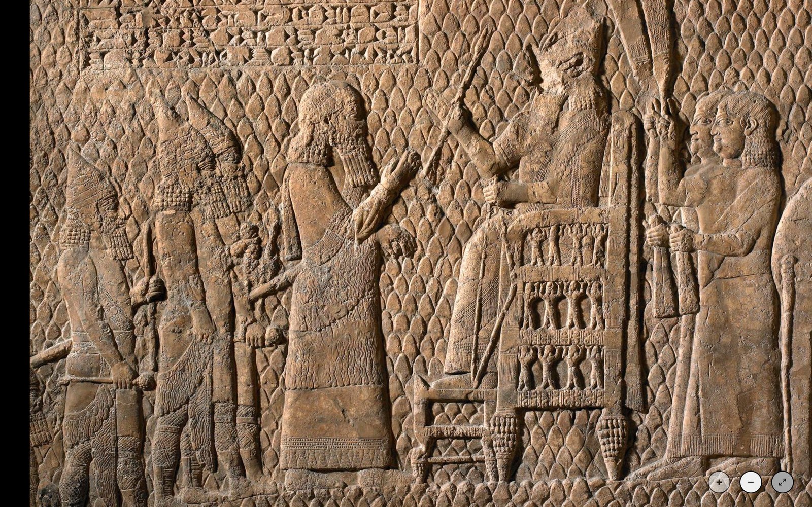 A carved stone palace relief: a bearded king seated on a high ornate throne receives bowing figures and prisoners, with dense cuneiform above.