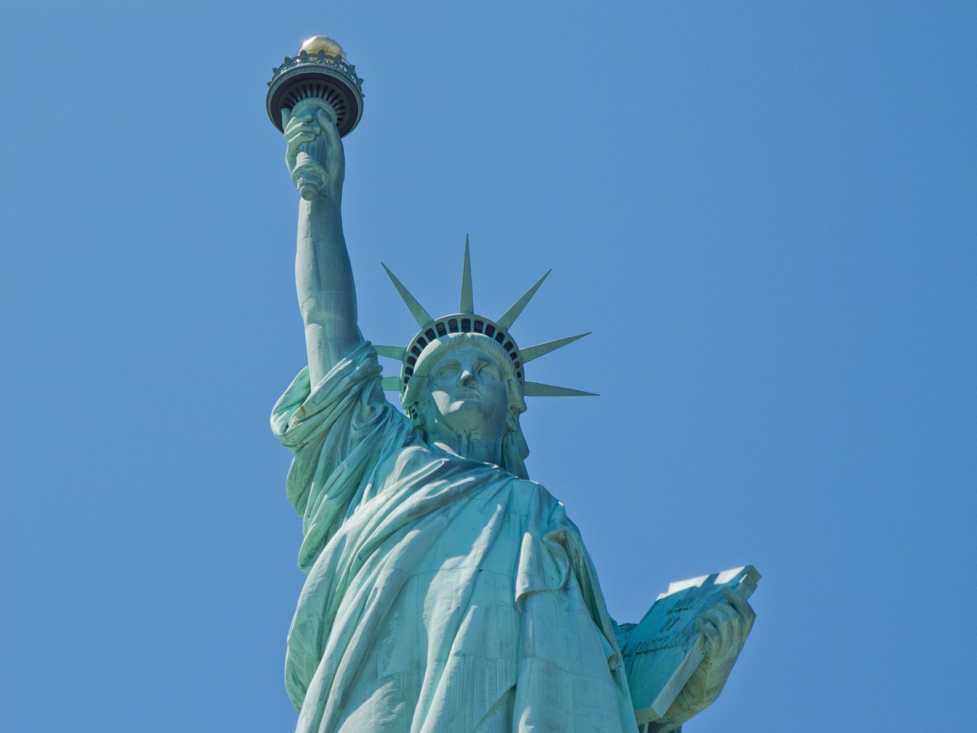 The Statue of Liberty against the sky, torch raised, photographed from below