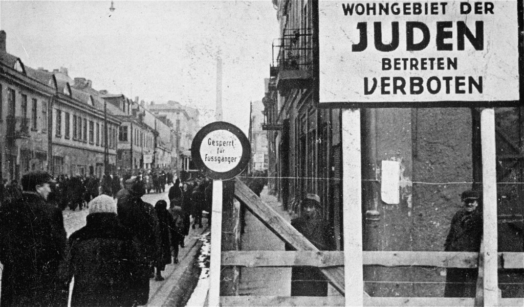 A German postcard of a Lodz ghetto boundary: a large sign reading Wohngebiet der Juden, Betreten verboten (Residential area of the Jews, entry forbidden) over a wooden barrier, with a crowded street behind.