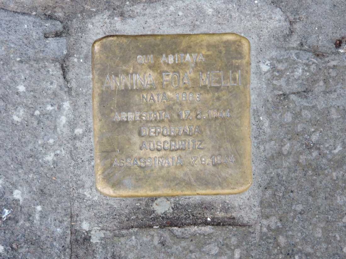 A brass Stolperstein set among cobblestones, engraved with the name and fate of a deported Jewish woman