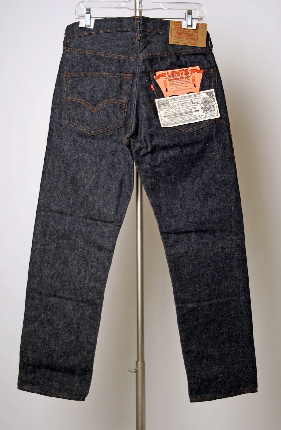 A new pair of dark blue Levi&rsquo;s 501 jeans seen from the back on a hanger, paper sales tags and a folded printed guarantee ticket tucked in the back pocket