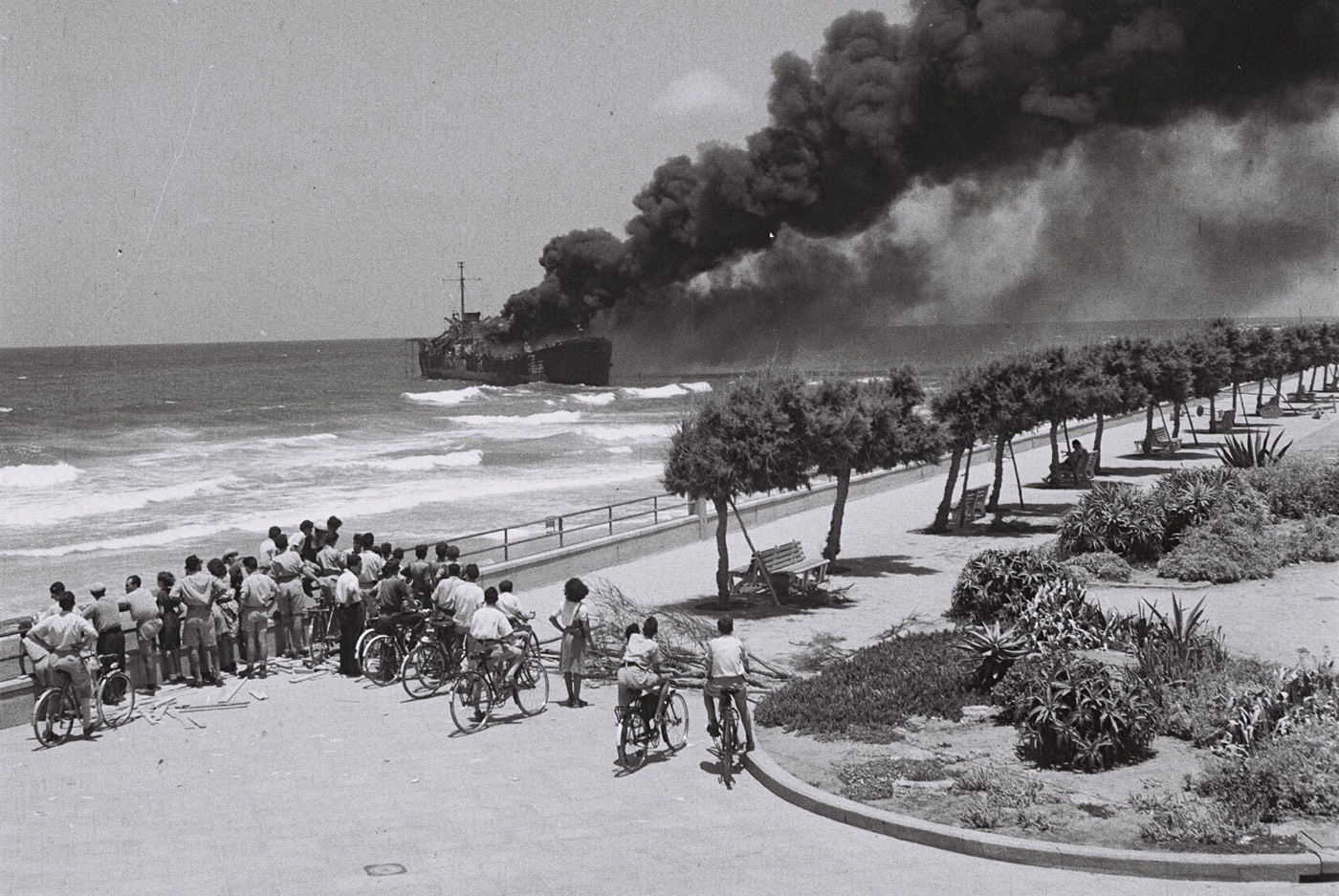 The cargo ship Altalena burning off the Tel Aviv shore in June 1948, smoke rising over the water, seen from the beach.