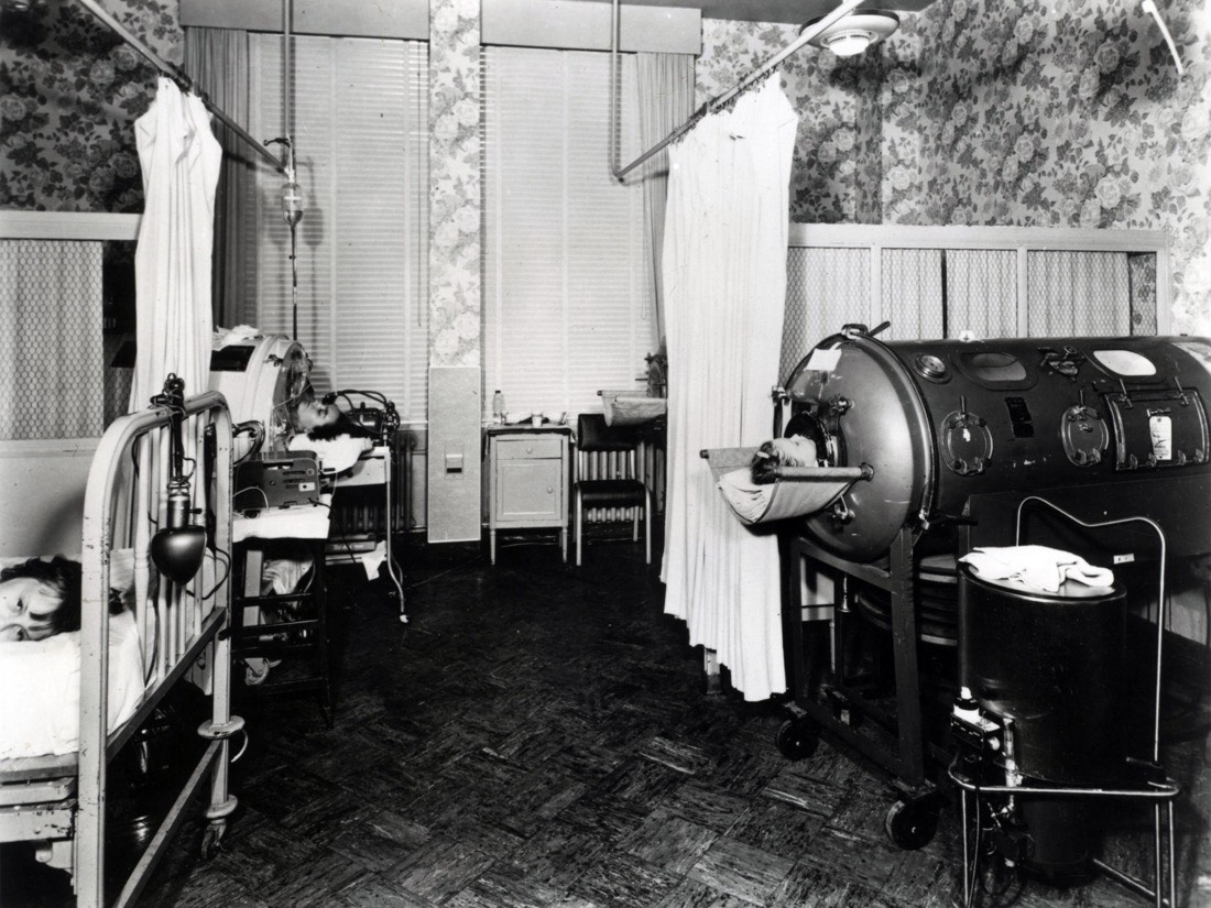 A yellow-green iron lung, a long metal cylinder on wheels with portholes and gauges, the machine that breathed for polio patients.