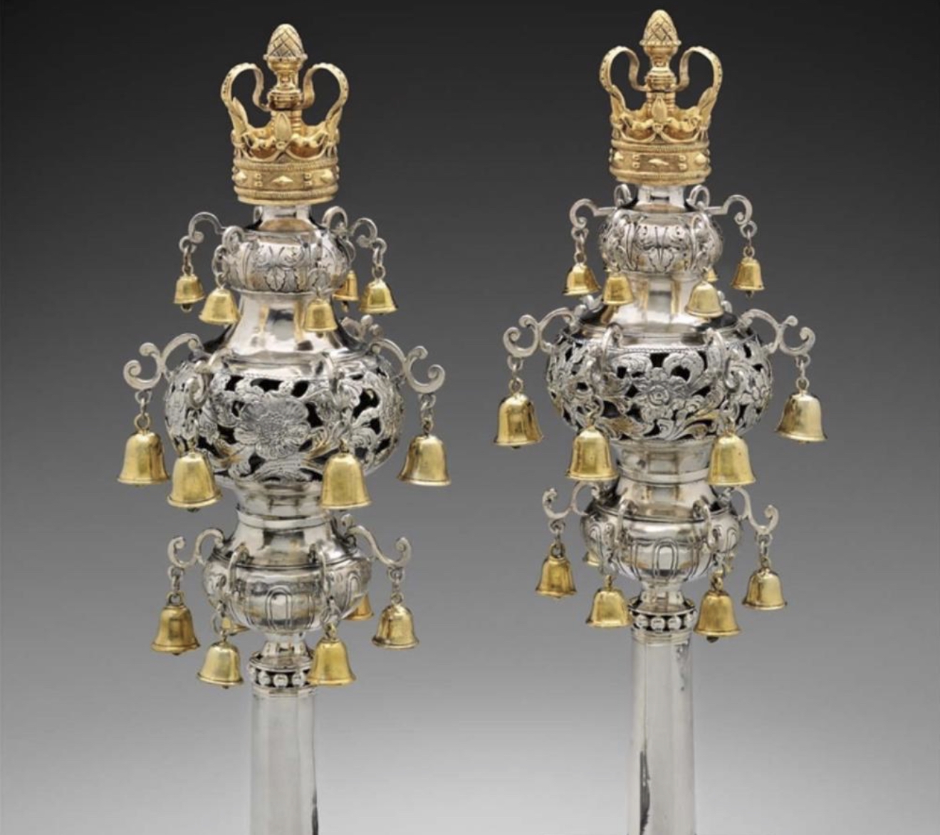 A pair of eighteenth-century silver Torah finials by Myer Myers, bulbous pierced silver bodies hung with small gold bells, each topped with a gold crown, made to crown the wooden staves of a Torah scroll.