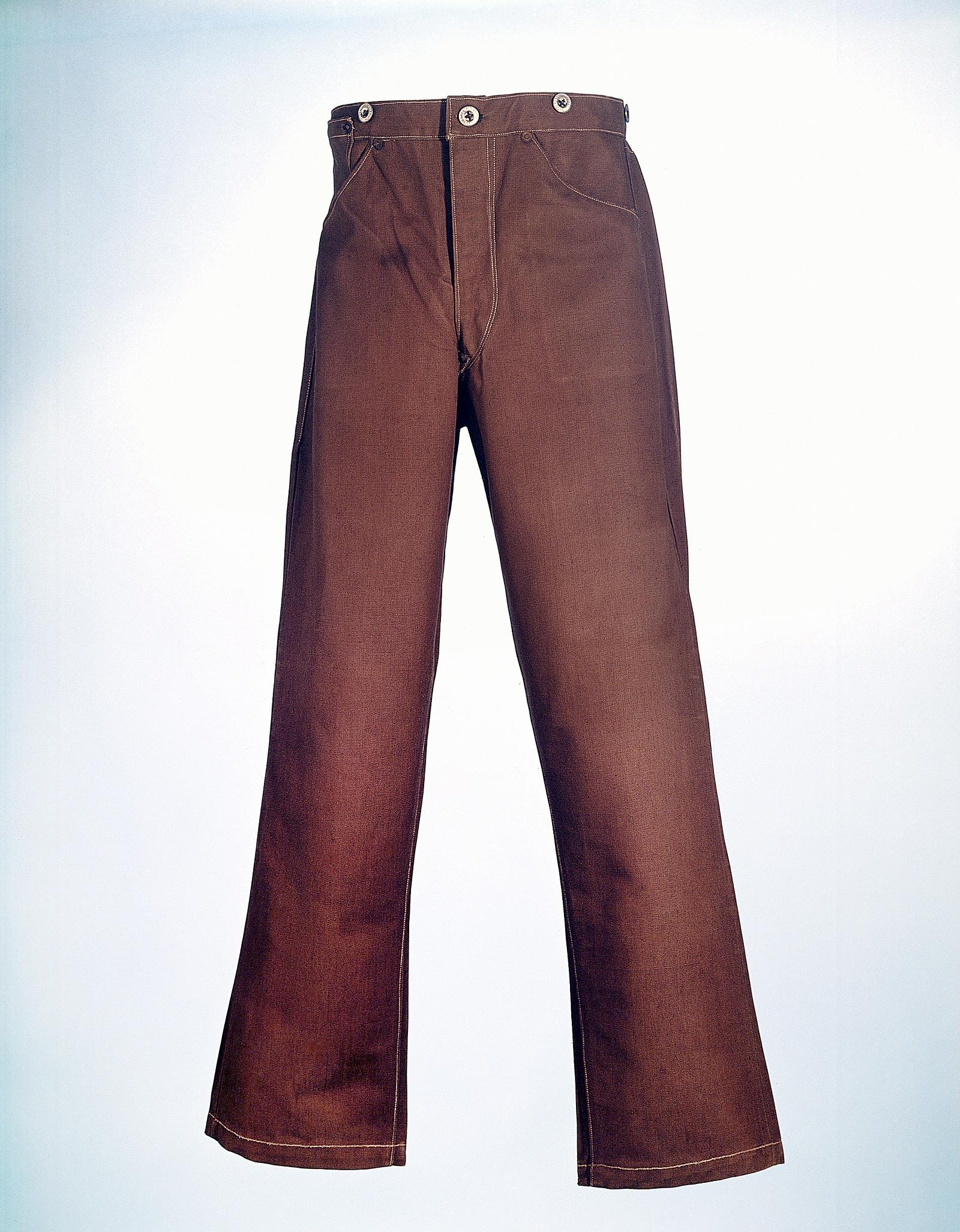 A worn pair of brown cotton duck work trousers from the late nineteenth century, photographed against a pale background, with metal buttons at the waist