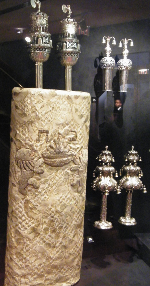 An embroidered Torah mantle on a scroll, topped with silver finials