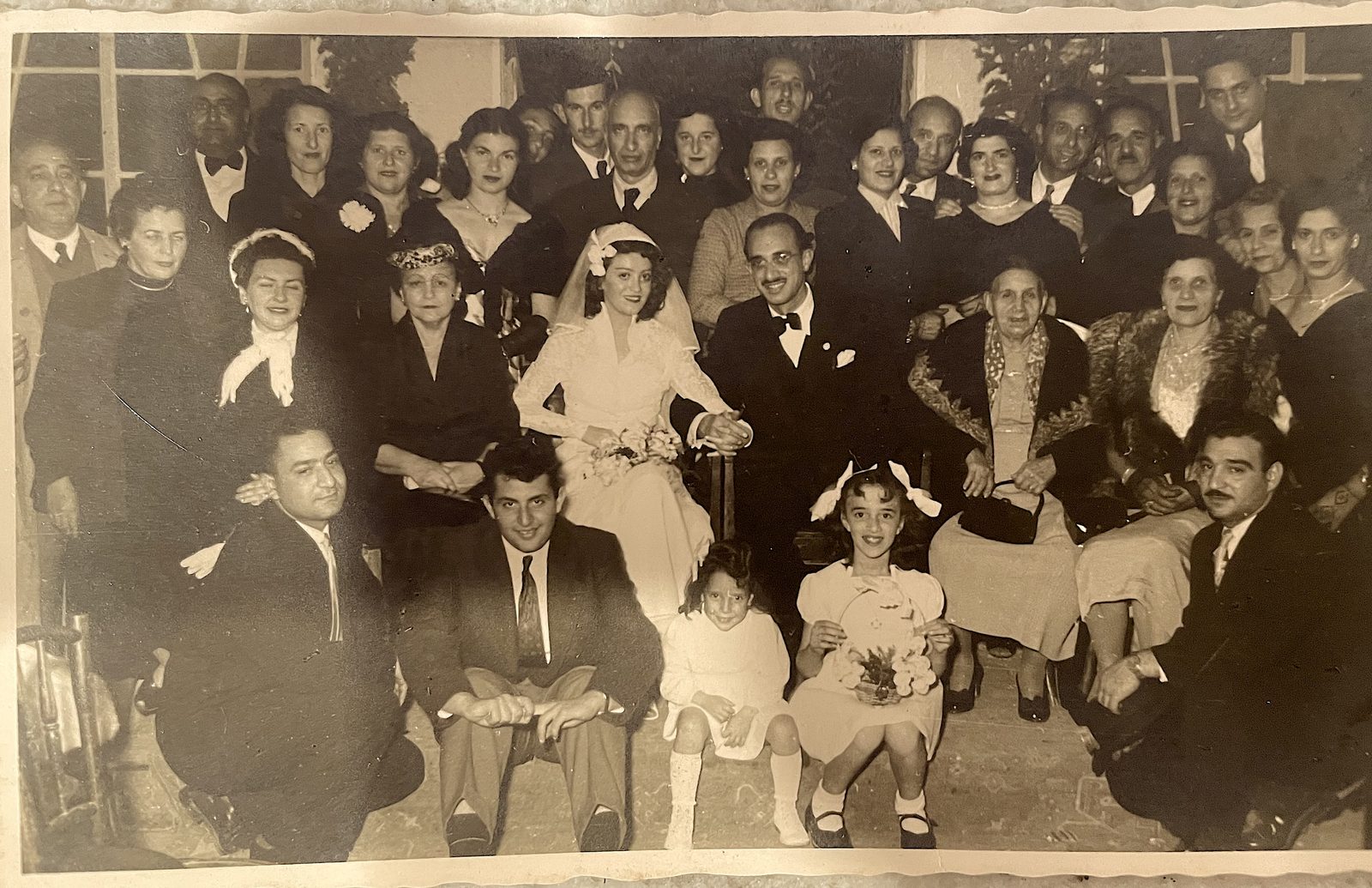 A Jewish wedding photographed in Israel in 1954: the bride in white and groom seated at the center, surrounded by three generations of family in formal dress.