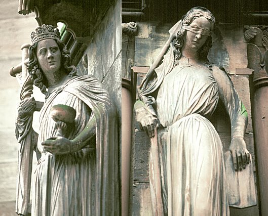 Two carved female figures in their cathedral setting: on the left a crowned woman standing upright holding a staff and an orb; on the right a woman with head tilted and eyes bound by a cloth blindfold, holding a broken staff, her body curving away.