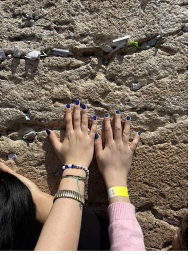Close-up of hands pressing folded paper notes into the gaps between the massive ancient stones of the Western Wall.